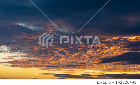 夕焼けのオレンジ色に照らされた層状の暗い雲と劇的な空 142326449