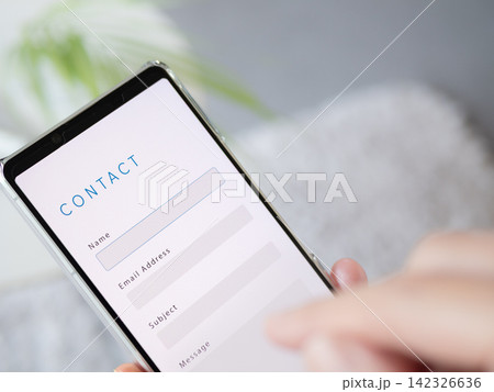 Webサイトのお問い合わせフォームからメッセージを送信する手元写真 (スマホ画面内はオリジナル制作) Webサイトのお問い合わせフォームからメッセージを送信する手元写真 (スマホ画面内はオリジナル制作) 142326636