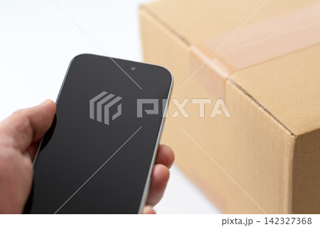 段ボールの荷物とスマホを持つ手元 段ボールの荷物とスマホを持つ手元 142327368
