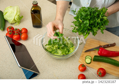 Cooking. Person adds fresh parsley to bowl of salad ingredients in stylish kitchen Cooking. Person adds fresh parsley to bowl of salad ingredients in stylish kitchen 142328187