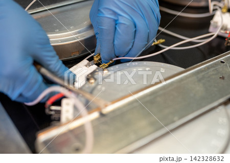 Closeup of gloved hands connecting wires to metal component in technical device 142328632