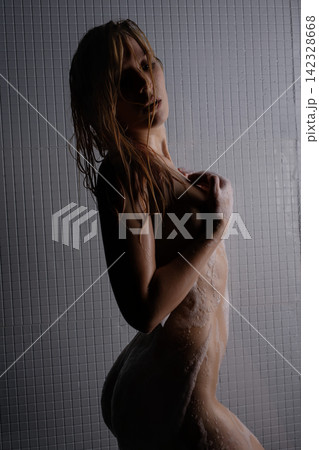 Woman showering with wet hair and soap suds against tiled wall Woman showering with wet hair and soap suds against tiled wall 142328668