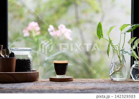 Coffee glass cup and roasted coffee beans on wooden table with flowers background 142329383