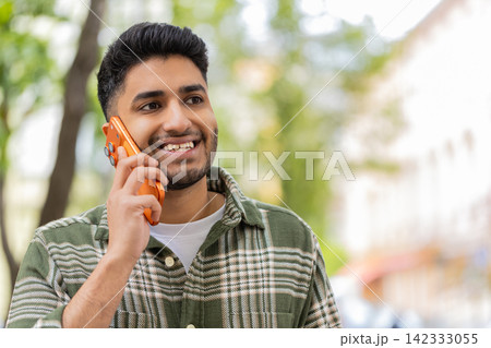 Indian man listening on smartphone walking in city street smiling while nodding during pleasant call 142333055