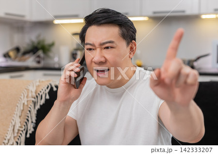Asian man argues on smartphone frowns shows no no finger gesture speaks firmly and rejects request Asian man argues on smartphone frowns shows no no finger gesture speaks firmly and rejects request 142333207