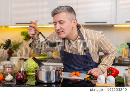 Middle-aged man smelling warm homemade soup in kitchen during healthy diet meal preparation at home Middle-aged man smelling warm homemade soup in kitchen during healthy diet meal preparation at home 142333240