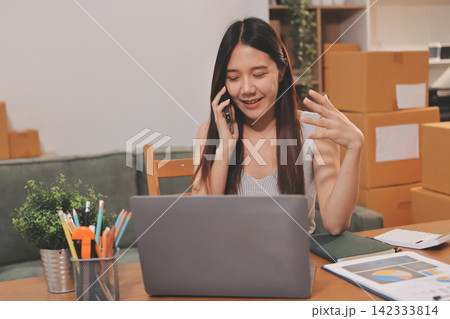 Startup SME small business entrepreneur of freelance Asian woman wearing apron using laptop and box to receive and review orders online to prepare to pack sell to customers, online sme business ideas. Startup SME small business entrepreneur of freelance Asian woman wearing apron using laptop and box to receive and review orders online to prepare to pack sell to customers, online sme business ideas. 142333814