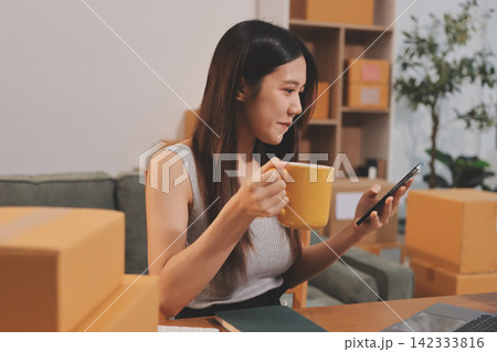 Startup SME small business entrepreneur of freelance Asian woman wearing apron using laptop and box to receive and review orders online to prepare to pack sell to customers, online sme business ideas. Startup SME small business entrepreneur of freelance Asian woman wearing apron using laptop and box to receive and review orders online to prepare to pack sell to customers, online sme business ideas. 142333816