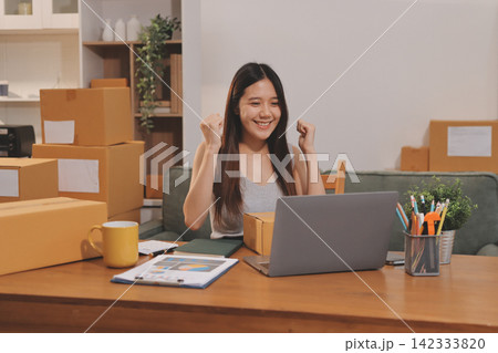Startup SME small business entrepreneur of freelance Asian woman wearing apron using laptop and box to receive and review orders online to prepare to pack sell to customers, online sme business ideas. Startup SME small business entrepreneur of freelance Asian woman wearing apron using laptop and box to receive and review orders online to prepare to pack sell to customers, online sme business ideas. 142333820