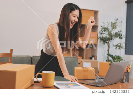 Startup SME small business entrepreneur of freelance Asian woman wearing apron using laptop and box to receive and review orders online to prepare to pack sell to customers, online sme business ideas. Startup SME small business entrepreneur of freelance Asian woman wearing apron using laptop and box to receive and review orders online to prepare to pack sell to customers, online sme business ideas. 142333822