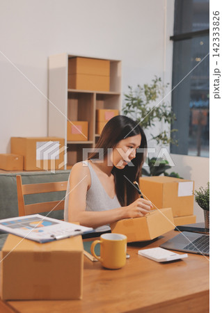 Startup SME small business entrepreneur of freelance Asian woman wearing apron using laptop and box to receive and review orders online to prepare to pack sell to customers, online sme business ideas. Startup SME small business entrepreneur of freelance Asian woman wearing apron using laptop and box to receive and review orders online to prepare to pack sell to customers, online sme business ideas. 142333826