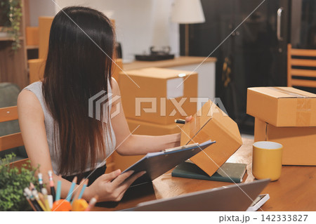 Startup SME small business entrepreneur of freelance Asian woman wearing apron using laptop and box to receive and review orders online to prepare to pack sell to customers, online sme business ideas. Startup SME small business entrepreneur of freelance Asian woman wearing apron using laptop and box to receive and review orders online to prepare to pack sell to customers, online sme business ideas. 142333827