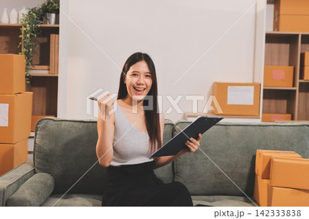 Startup SME small business entrepreneur of freelance Asian woman wearing apron using laptop and box to receive and review orders online to prepare to pack sell to customers, online sme business ideas. Startup SME small business entrepreneur of freelance Asian woman wearing apron using laptop and box to receive and review orders online to prepare to pack sell to customers, online sme business ideas. 142333838