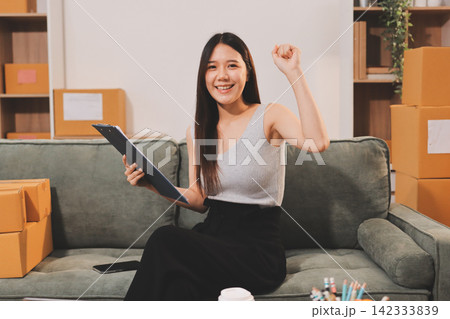 Startup SME small business entrepreneur of freelance Asian woman wearing apron using laptop and box to receive and review orders online to prepare to pack sell to customers, online sme business ideas. Startup SME small business entrepreneur of freelance Asian woman wearing apron using laptop and box to receive and review orders online to prepare to pack sell to customers, online sme business ideas. 142333839
