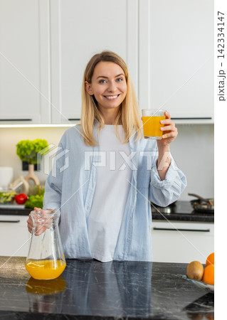 Young woman pouring fresh orange juice into glass for healthy fit breakfast vitamins in home kitchen 142334147