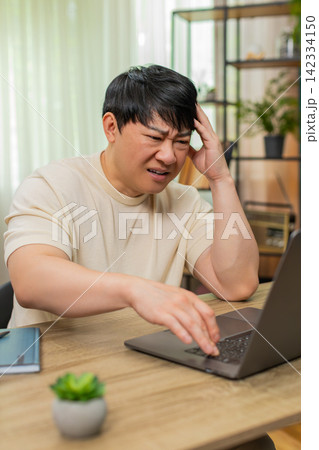 Asian man angrily rereading email on laptop, tapping keyboard, tense face after receiving bad news Asian man angrily rereading email on laptop, tapping keyboard, tense face after receiving bad news 142334150