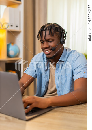 African American young man on home table assisting client online as call center agent with headset 142334275