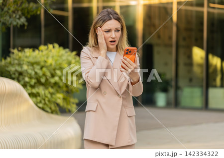 Young woman checking rejected deal message while walking in city street feeling shocked and alarmed Young woman checking rejected deal message while walking in city street feeling shocked and alarmed 142334322