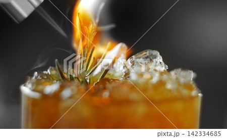 Flaming cocktail with burning rosemary twig and ice creating smoke, showing unique mixology craftsmanship 142334685