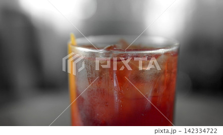 Cold red cocktail with ice cubes and orange garnish, condensation forming on the glass, showing a refreshing drink Cold red cocktail with ice cubes and orange garnish, condensation forming on the glass, showing a refreshing drink 142334722