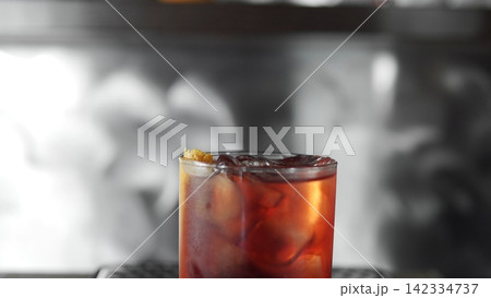 Negroni cocktail with ice cubes and orange peel garnish, reflecting lighting in a dark bar setting Negroni cocktail with ice cubes and orange peel garnish, reflecting lighting in a dark bar setting 142334737