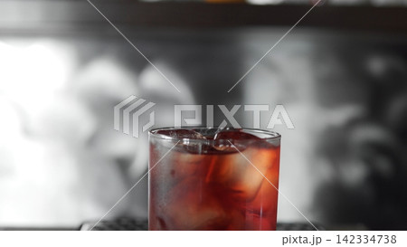 Glass of iced red cocktail on a bar counter, refreshing cold drink for a party or celebration Glass of iced red cocktail on a bar counter, refreshing cold drink for a party or celebration 142334738