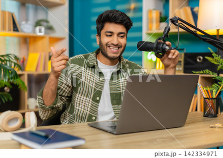 Indian man on home table recording video blog with microphone on laptop sharing advice tips online Indian man on home table recording video blog with microphone on laptop sharing advice tips online 142334971