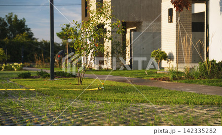 Lawn sprinkler watering green grass in a modern suburban backyard garden, providing automatic irrigation for plants Lawn sprinkler watering green grass in a modern suburban backyard garden, providing automatic irrigation for plants 142335282