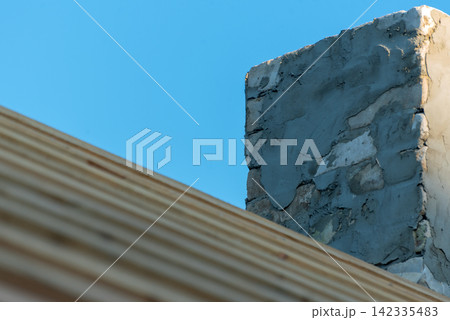 Rough brick and cement wall of a building rises above a blurred wooden beam, weathered masonry texture contrasting with a clear, vibrant blue sky on a sunny day 142335483