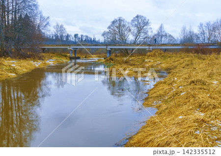 Low concrete bridge over calm river in late winter rural landscape with golden reeds Low concrete bridge over calm river in late winter rural landscape with golden reeds 142335512