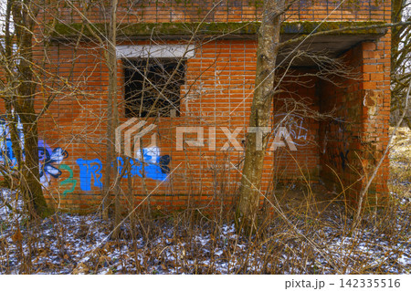 Abandoned brick building covered with graffiti, open doorway and leafless shrubs in wintry foreground Abandoned brick building covered with graffiti, open doorway and leafless shrubs in wintry foreground 142335516