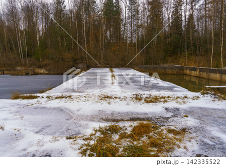 Snow dusted concrete pier extending into frozen pond with leafless birch forest background Snow dusted concrete pier extending into frozen pond with leafless birch forest background 142335522