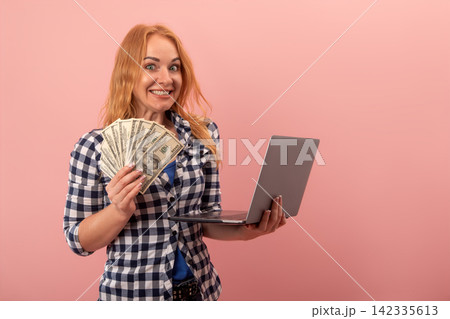 Happy woman holding a fan of dollar bills and a laptop, cheerfully reacting to making money through online work, representing financial freedom and digital business success Happy woman holding a fan of dollar bills and a laptop, cheerfully reacting to making money through online work, representing financial freedom and digital business success 142335613