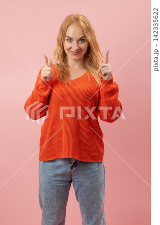 Young woman standing confidently, pointing both index fingers upwards against a pink background, conveying a playful and directing demeanor Young woman standing confidently, pointing both index fingers upwards against a pink background, conveying a playful and directing demeanor 142335622
