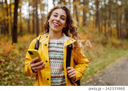 Hiking in autumn forest. Smiling tourist in bright coat walks through autumn park in sunny weather. 142335668