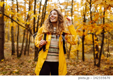 Hiking in autumn forest. Smiling tourist in bright coat walks through autumn park in sunny weather. 142335670