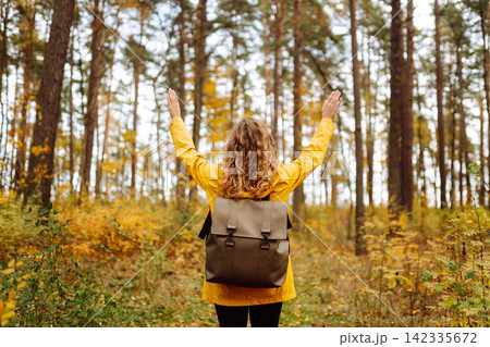 Back view. Curly woman with backpack in autumn forest enjoying nature. Concept of relaxation, nature Back view. Curly woman with backpack in autumn forest enjoying nature. Concept of relaxation, nature 142335672
