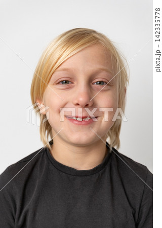 Blond young boy with a cheerful facial expression is smiling confidently at the camera, portraying feelings of joy, childhood, and positive optimism 142335778