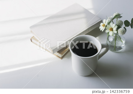 朝の柔らかな光の中のコーヒーと本と白い花 142336759