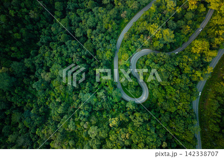 Aerial view of a winding road through a lush green forest with a driving car. Aerial view of a winding road through a lush green forest with a driving car. 142338707
