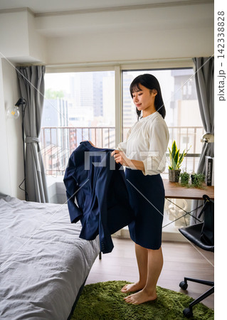 スーツを手に持ち、部屋で身支度をする女性 度をする女性 スーツを手に持ち、部屋で身支度をする女性 度をする女性 142338828