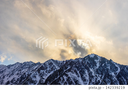 Dramatic Snow-Capped Mountain Peaks Under Sunlit Clouds 142339219