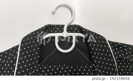 Black polka dot clothes hanging on a white plastic hanger, a garment with a classic collar, contrast trim and an elegant vintage style 142339648