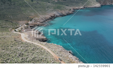 Aerial view of a winding coastal road approaching Ombros Gialos Bay in Crete, featuring clear turquoise waters, rocky cliffs, and verdant hills, creating a picturesque natural landscape Aerial view of a winding coastal road approaching Ombros Gialos Bay in Crete, featuring clear turquoise waters, rocky cliffs, and verdant hills, creating a picturesque natural landscape 142339901