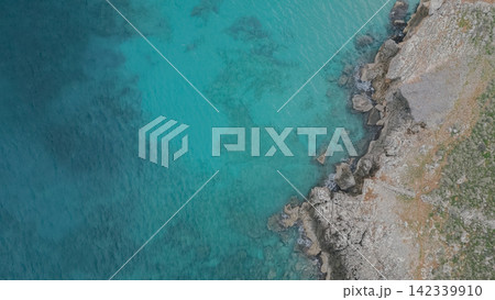Aerial perspective of a rugged coastline where rocky formations meet the vibrant turquoise waters of the Mediterranean Sea in Crete, highlighting the natural beauty of the region Aerial perspective of a rugged coastline where rocky formations meet the vibrant turquoise waters of the Mediterranean Sea in Crete, highlighting the natural beauty of the region 142339910