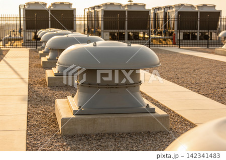 Industrial rooftop ventilation units lined up under the warm glow of sunset 142341483