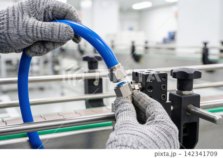 Worker connects pneumatic tube fitting on industrial conveyor system Worker connects pneumatic tube fitting on industrial conveyor system 142341709