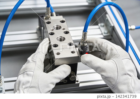 Technician wearing gloves installs pneumatic valve manifold in industrial automation setup Technician wearing gloves installs pneumatic valve manifold in industrial automation setup 142341739