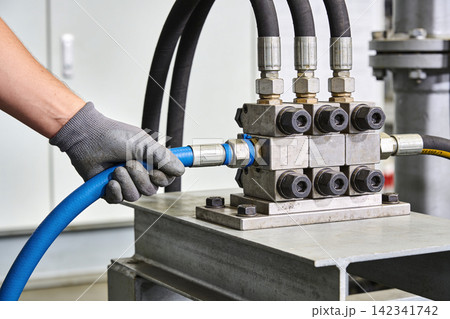 Worker connects blue hydraulic hose to complex valve manifold system in industrial setting Worker connects blue hydraulic hose to complex valve manifold system in industrial setting 142341742