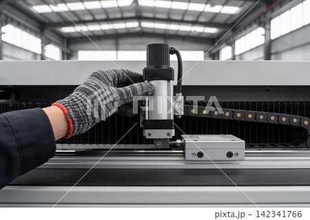 Worker in protective glove adjusts industrial machine component in a factory setting 142341766